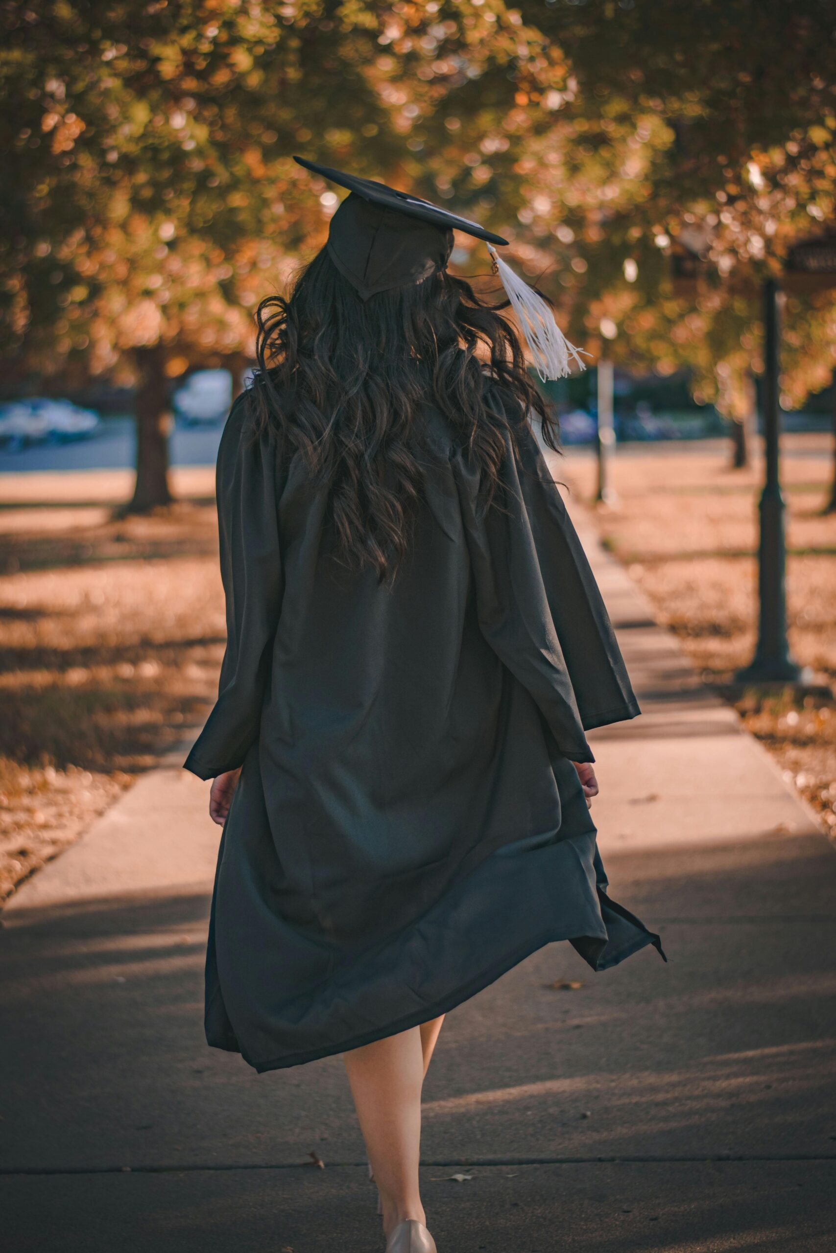 Study Abroad Back view of a graduate walking in an autumn park in academic dress.